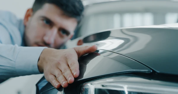 Un homme examine attentivement la carrosserie d'un véhicule en passant sa main sur la surface métallique peinte