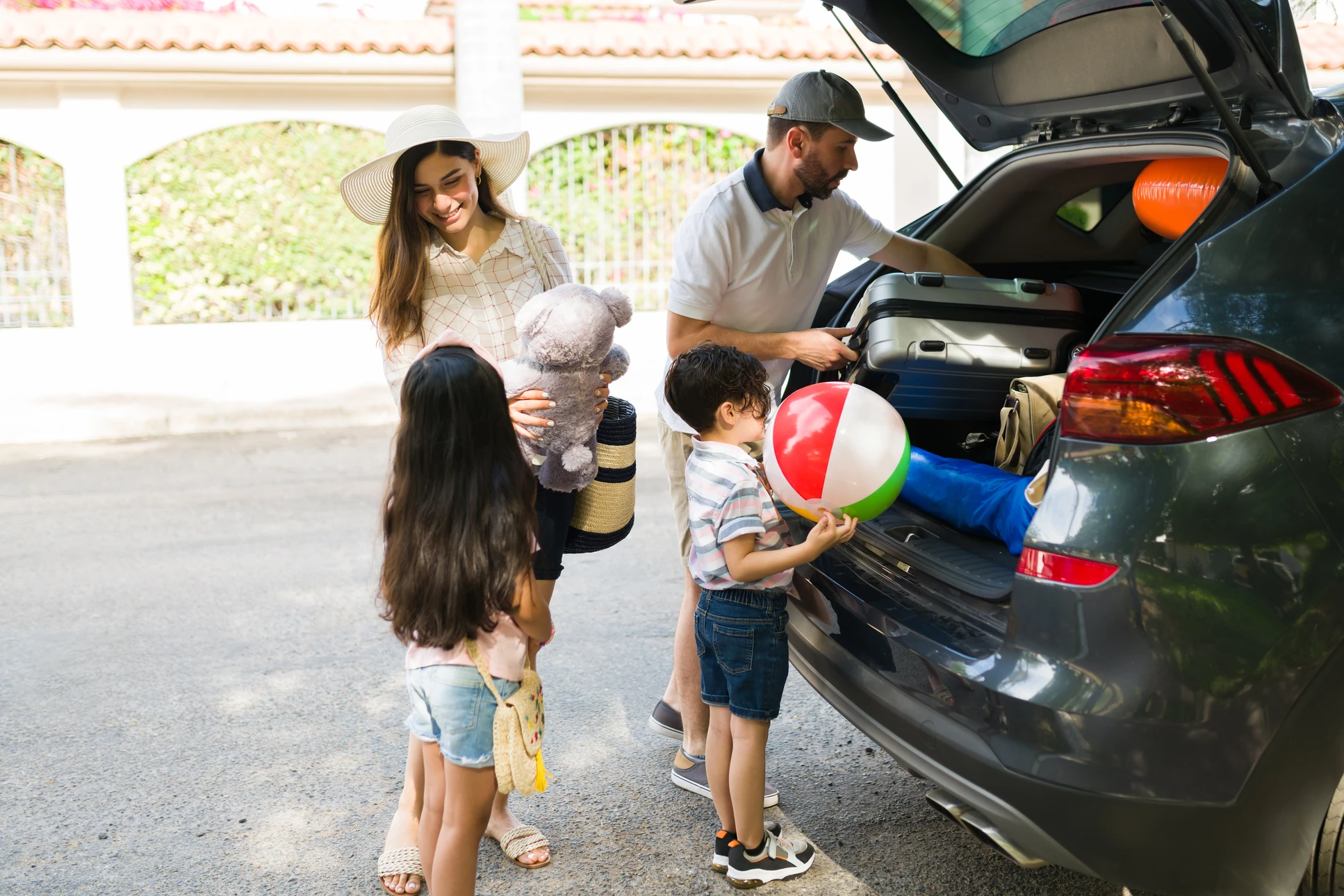 Famille préparant voyage en voiture, parents et deux enfants chargeant coffre SUV avec bagages, jouets et équipements vacances
