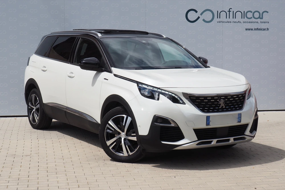 SUV blanc Peugeot 5008 de seconde génération, photographié en extérieur sur fond de mur gris d'un concessionnaire Infinicar