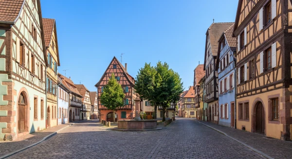 Vue d'une rue ou place principale de Benfeld avec des bâtiments caractéristiques de la commune, photographiée en journée avec une bonne luminosité, montrant un environnement urbain ou semi-urbain typique de la région alsacienne. L'image doit transmettre un sentiment de localisation géographique précise et de proximité, sans nécessairement montrer des véhicules ou des activités commerciales.