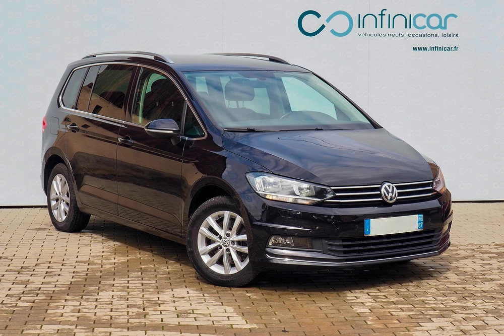 Monospace Volkswagen Touran noir profond photographié de trois quarts avant gauche sur parking pavé