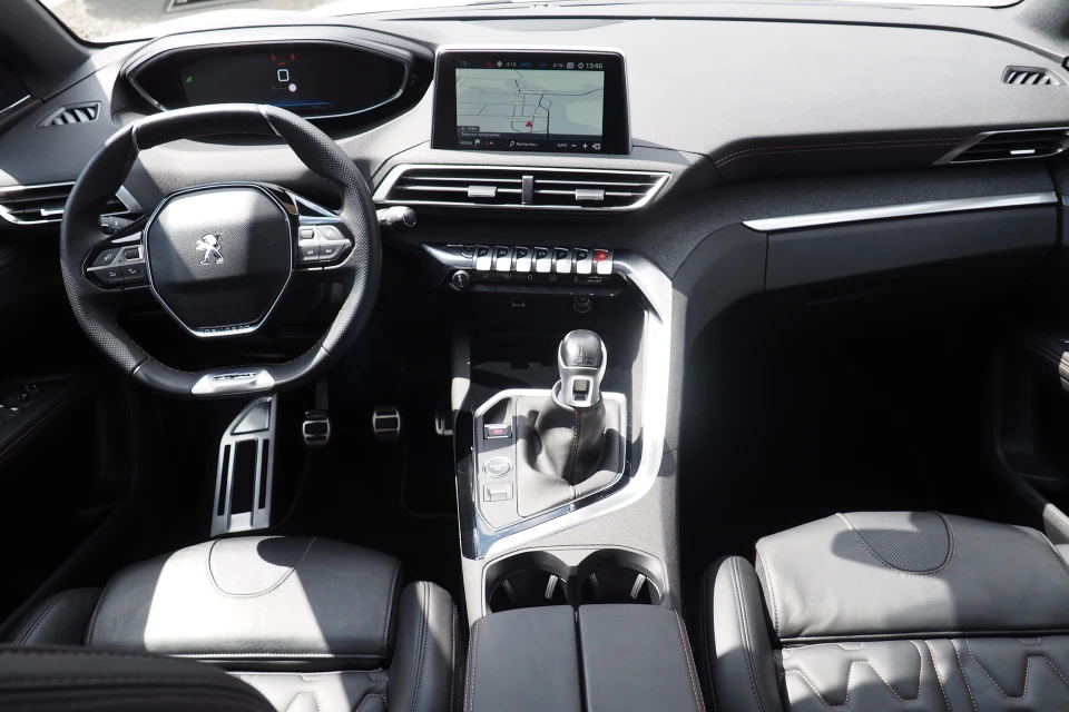 Intérieur d'un véhicule automobile où un vendeur en chemise bleue présente les fonctionnalités du tableau de bord à un client assis au volant en chemise blanche