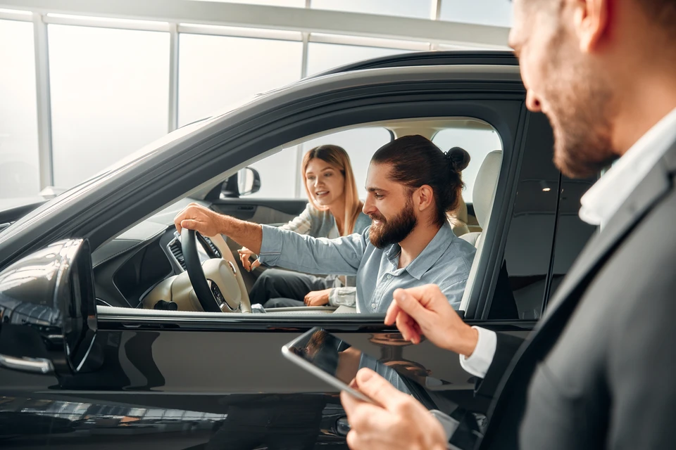 Atelier automobile moderne avec mécanicien en combinaison bleue consultant documents jaunes avec cliente en chemisier beige près d'un véhicule noir au capot ouvert